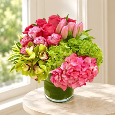 Pink roses, tulips, orchids, and hydrangeas in a glass vase