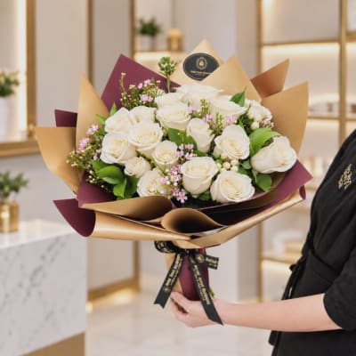 Bouquet of white roses with pink filler flowers wrapped in gold and burgundy paper