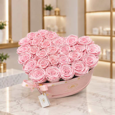 Pink roses arranged in a heart-shaped pink box with a ribbon