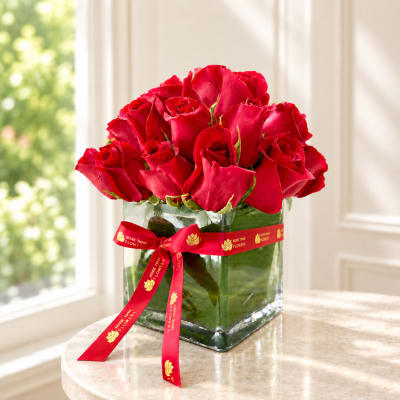 Red roses arranged in a clear square glass vase with a red ribbon