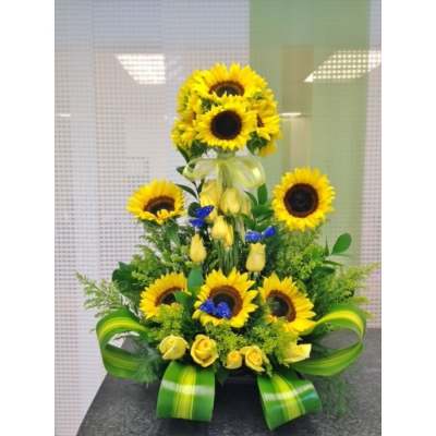Tall sunflower and yellow rose arrangement with blue butterfly accents and green ribbon in a low container