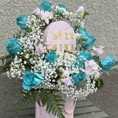 Pink memorial arrangement with blue roses and baby's breath around a name plaque