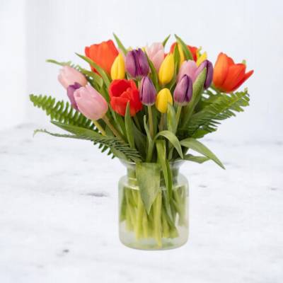 Mixed-color tulip bouquet with ferns arranged in a clear glass vase