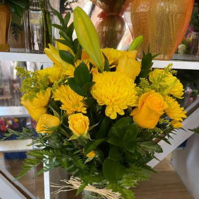 Tall arrangement of yellow roses, lilies, and chrysanthemums in a clear glass vase