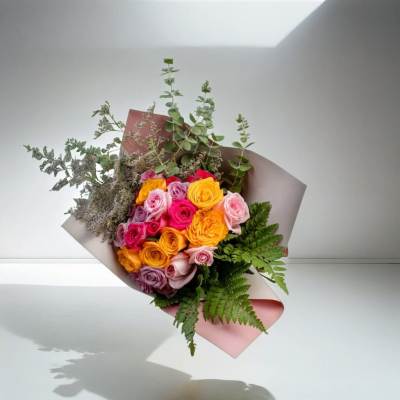 Hand-tied bouquet of pink, yellow, and lavender roses with greenery wrapped in blush paper