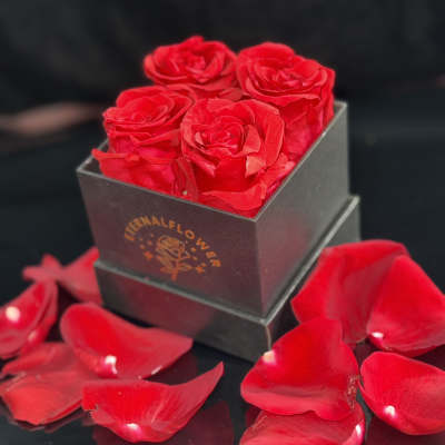 Red roses in a black square box with scattered rose petals