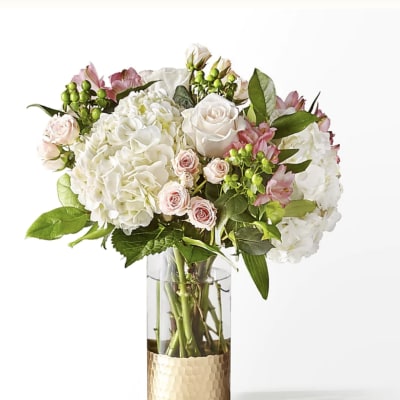 White and blush bouquet in a clear glass vase with a gold base