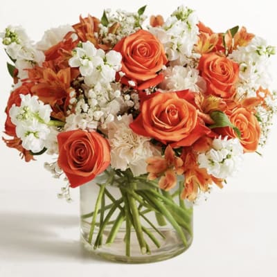Orange roses and white flowers arranged in a clear glass vase