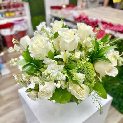Arrangement of white roses and other white blooms with green accent flowers in a low vase