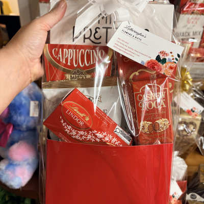 Red gift bag of cappuccino and chocolates wrapped in cellophane with a white bow.