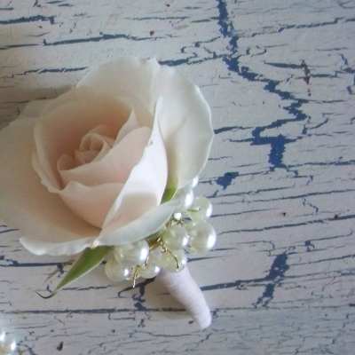 White rose boutonniere with pearl accents on a wrapped stem