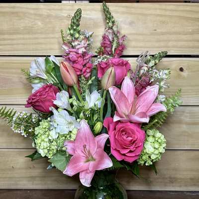 Pink lilies and roses arranged in a glass vase with white blooms