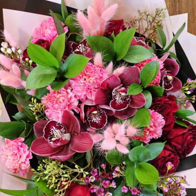 Bouquet of pink and burgundy flowers with green foliage and black-and-white wrap