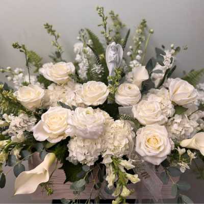 White roses and calla lilies arranged in a low box with greenery.