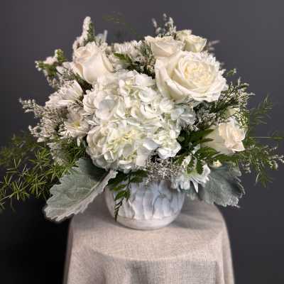 Low white arrangement of roses and hydrangeas in a white ceramic pot on a draped pedestal
