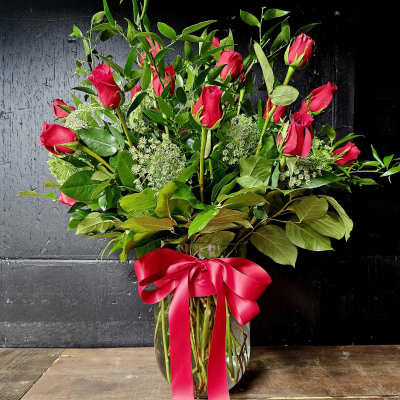 Red roses in a clear glass vase with a pink ribbon