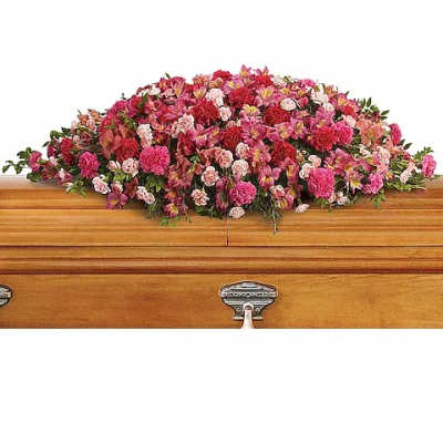 Pink and red casket spray of mixed flowers arranged on a light wood casket