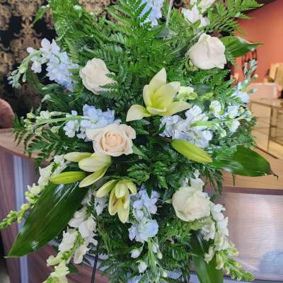 Standing floral spray with white roses, lilies, and pale blue blooms