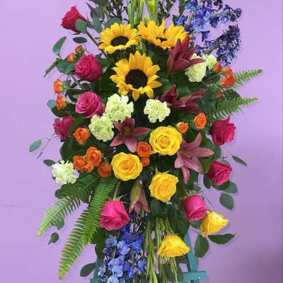 Tall standing floral spray with roses, sunflowers, lilies, and blue accents