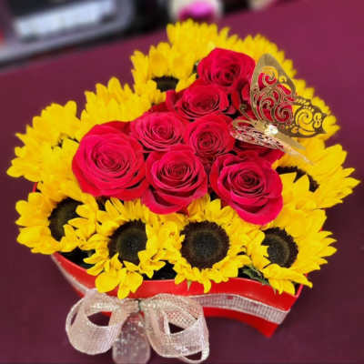 Red roses arranged with yellow sunflowers in a heart-shaped box