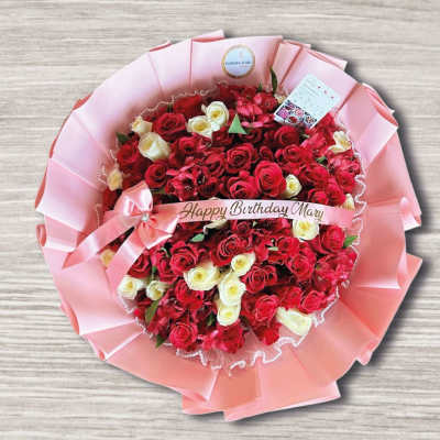 Round bouquet of red and white roses wrapped in pink paper with a birthday ribbon