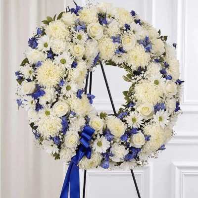 White and blue floral wreath on a stand with a blue ribbon