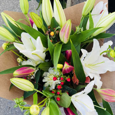 Bouquet of white and pink lilies with red berries wrapped in brown kraft paper