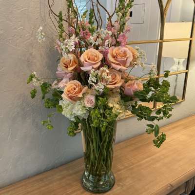 Peach and pink roses in a clear glass vase with airy white filler flowers