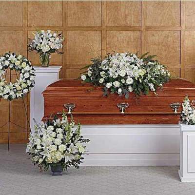 White funeral casket surrounded by white floral sprays and wreaths