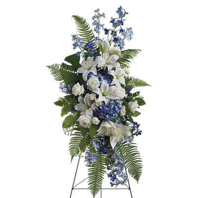 Standing floral spray with white lilies, roses, and blue flowers on an easel
