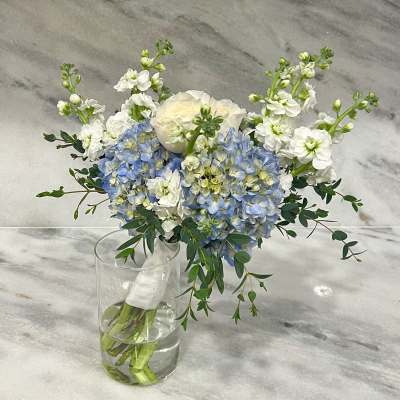 Hand-tied bouquet of blue hydrangeas, white stock, and ivory rose in a clear glass vase.