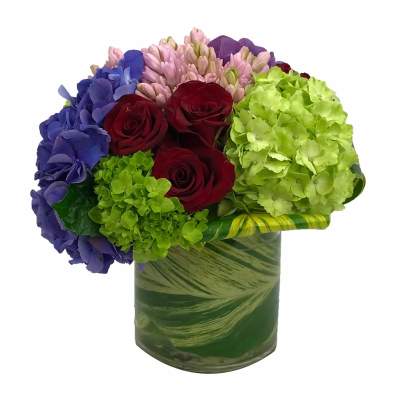 Bouquet of red roses, hydrangeas, and pink blooms in a green glass vase