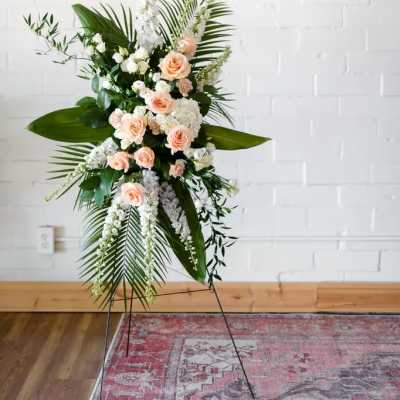 Peach roses and white flowers in a tall standing spray with palm leaves