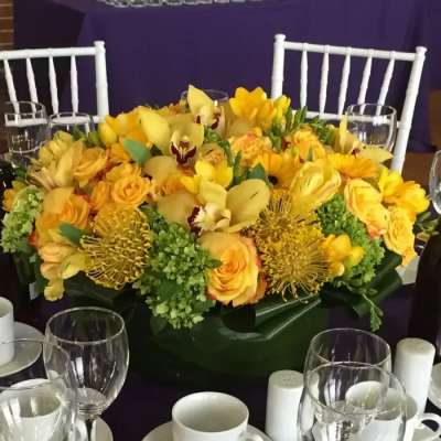 Yellow floral centerpiece in a low green container on a table