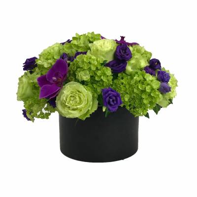 Green and purple floral arrangement in a black round container
