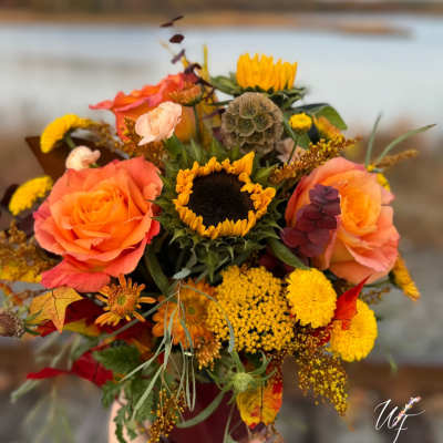 Bouquet with orange roses and a sunflower, held outdoors by water