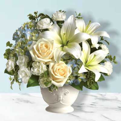 White lilies and cream roses in a white vase with blue hydrangeas
