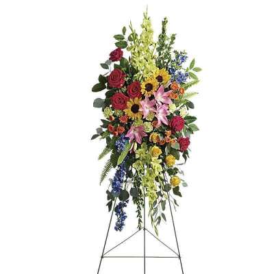 Tall standing floral spray with roses, lilies, sunflowers, and blue accents on an easel