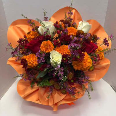 Bright bouquet of orange marigolds, red and white roses, and purple blooms wrapped in orange tissue