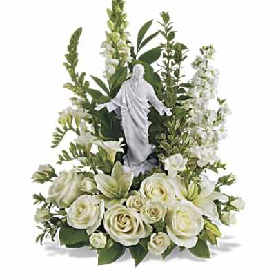 White religious figurine surrounded by white roses, lilies, and tall white flowers in an arrangement