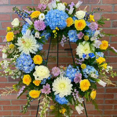 Large floral wreath on an easel with blue, yellow, white, and lavender blooms