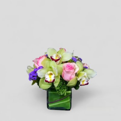 Pink roses and green orchids in a square glass vase