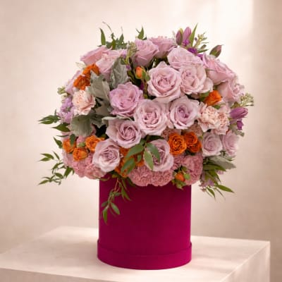 Lavender and peach roses with carnations in a bright pink hat box container