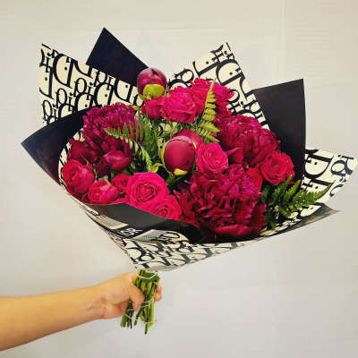 Handheld bouquet of hot pink roses and deep magenta blooms in patterned wrap