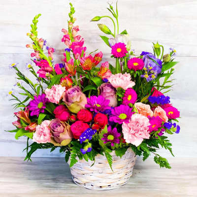 Mixed bouquet in a white wicker basket with pink, purple, and orange flowers
