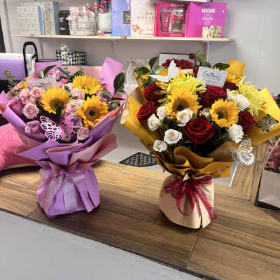 Two wrapped bouquets with sunflowers and roses on a counter