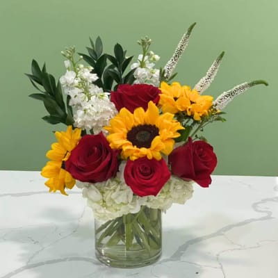 Bouquet of red roses, yellow sunflowers, and white flowers in a glass vase