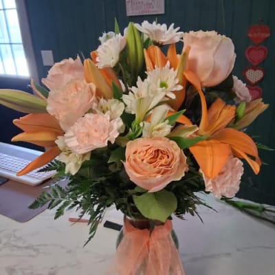 Peach and orange bouquet with lilies, roses, and white daisies in a glass vase