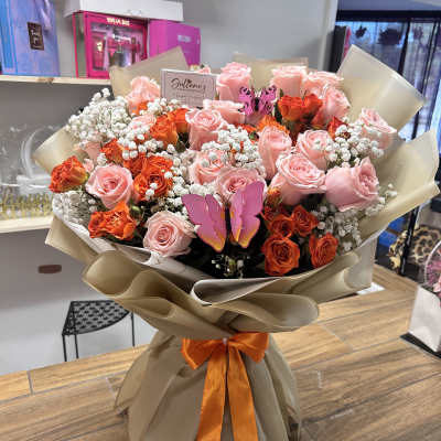 Bouquet of pink and orange roses with baby’s breath in tan wrap