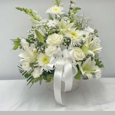 White floral arrangement with lilies, roses, and daisies in a round container
